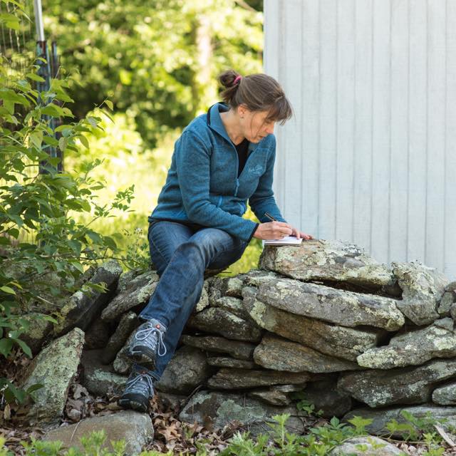 Chris Woodside writing notes while sitting on a stone wall